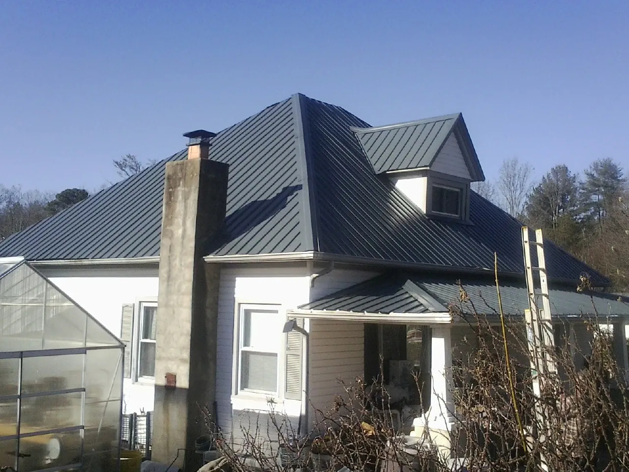 Dark blue standing seam metal roof on a white farmhouse with dormer — Slate & Tile Roof Repair by Roofing Brothers in East Grand Forks