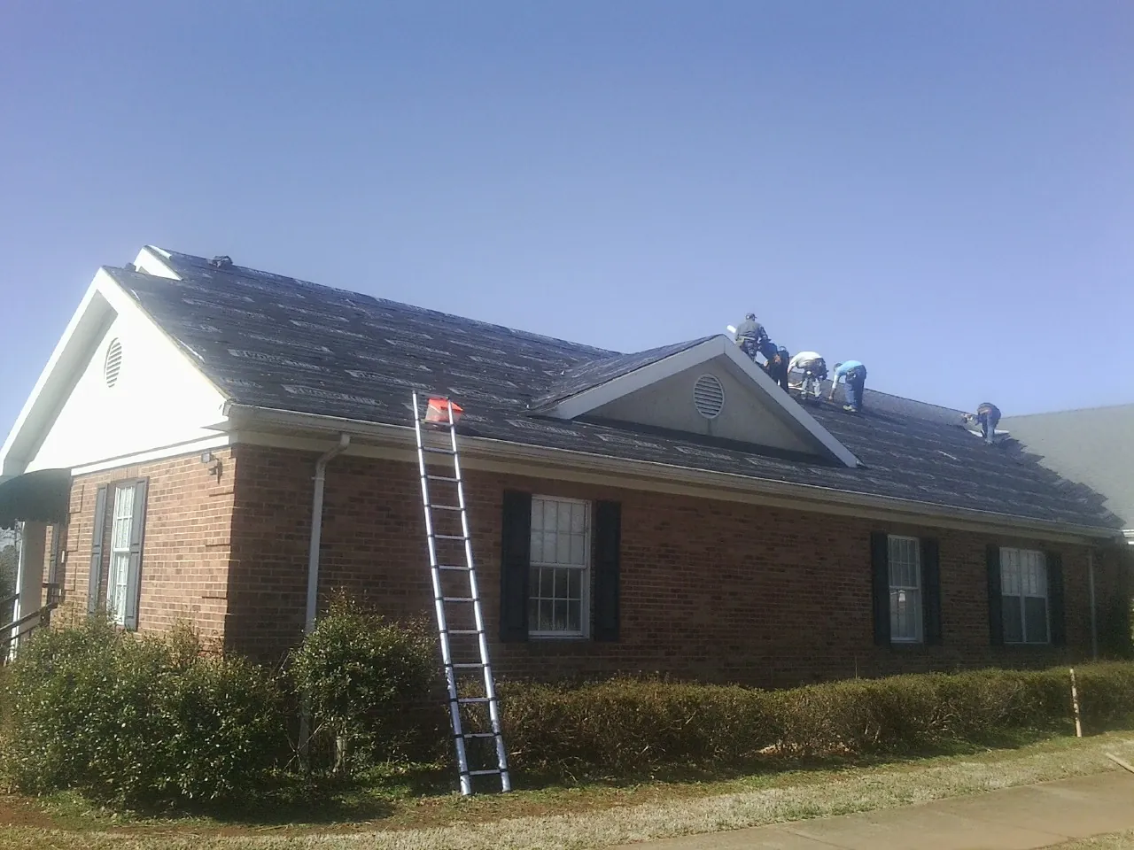 Crew tearing shingles off a brick ranch roof with a ladder set — Emergency Roof Repair work by our crew in East Grand Forks