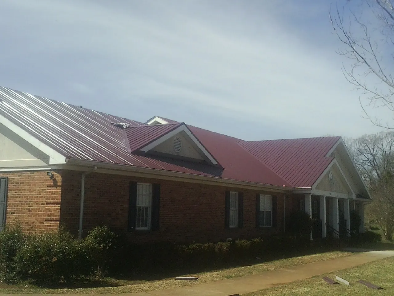 Red metal roof with gabled entries on a long brick building, from a Hail Damage Roof Repair job in East Grand Forks