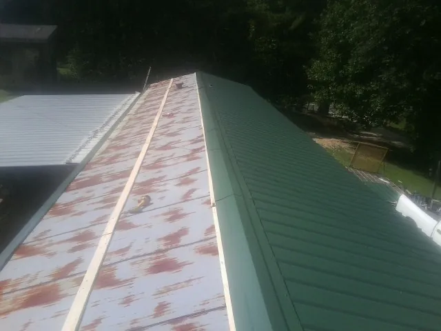 Old rusted panels beside newly installed green metal roofing — Wind Damage Roof Repair by Roofing Brothers in East Grand Forks