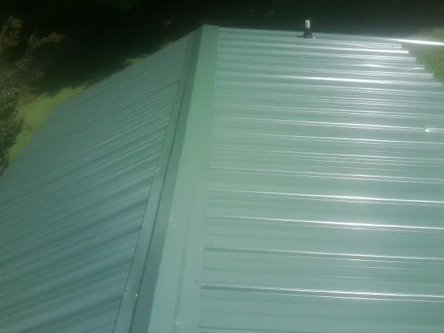 New green metal panels meeting at the ridge of a roof — Flat Roof Repair work by our crew in East Grand Forks
