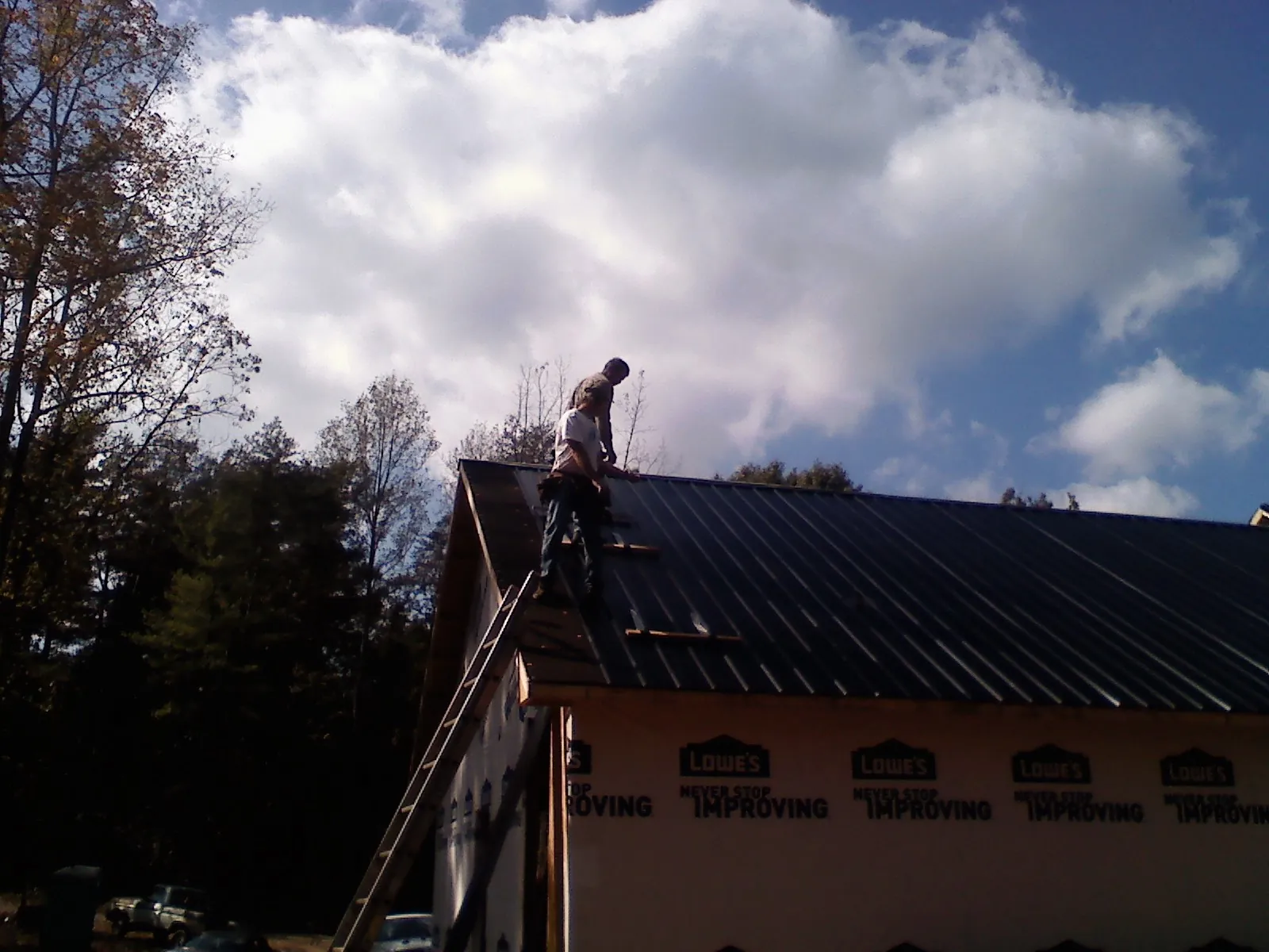 Roofer fastening dark metal panels high against a cloudy sky, from a Roof Inspection job in East Grand Forks