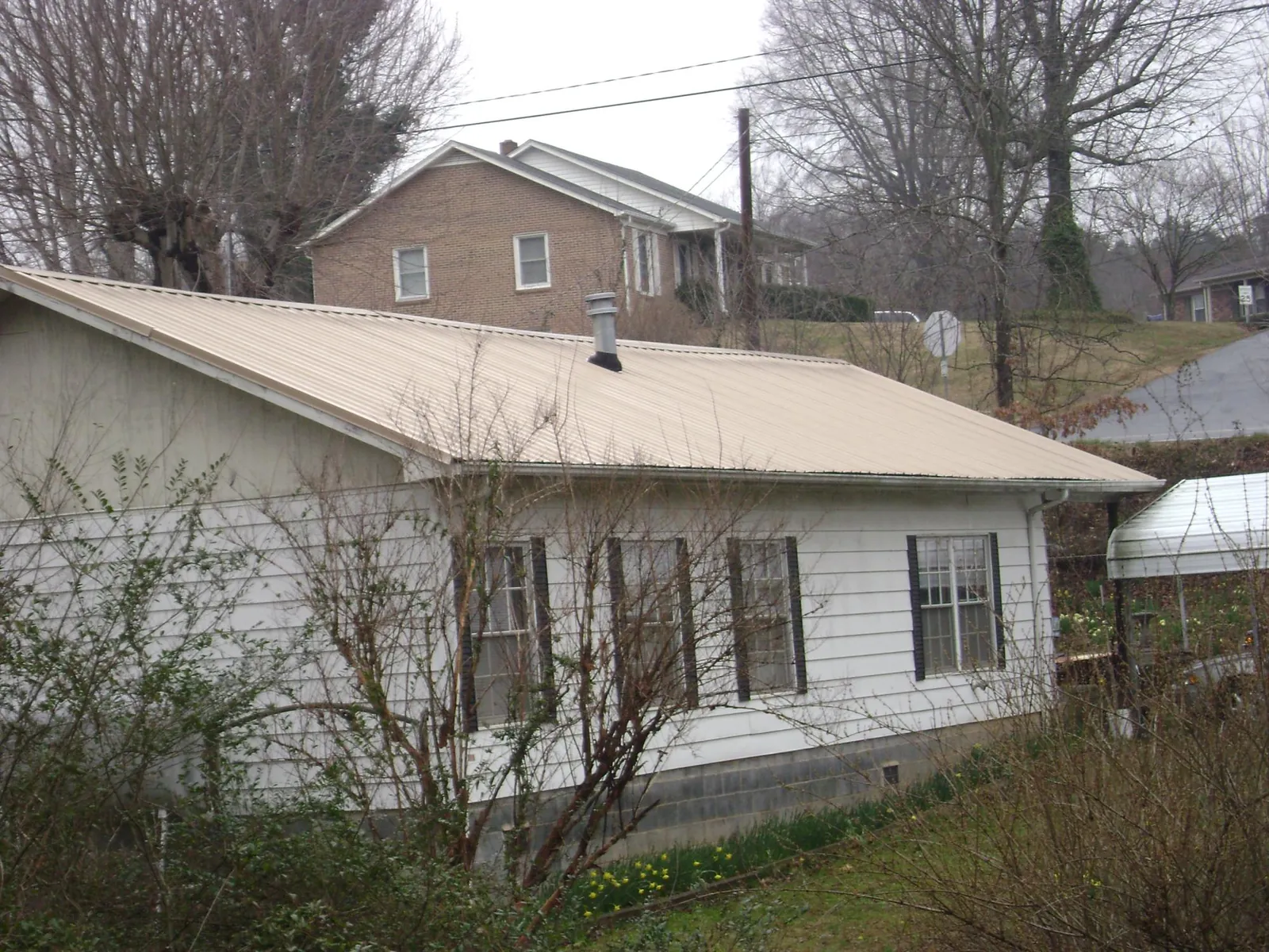 Tan metal roof on a white sided house set into a hillside — Commercial Roofing by Roofing Brothers in East Grand Forks