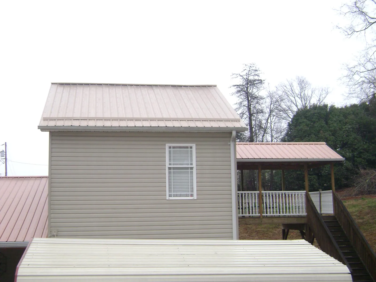 Tan metal roofs on a two story addition and attached porch, from a Roof Replacement job in East Grand Forks